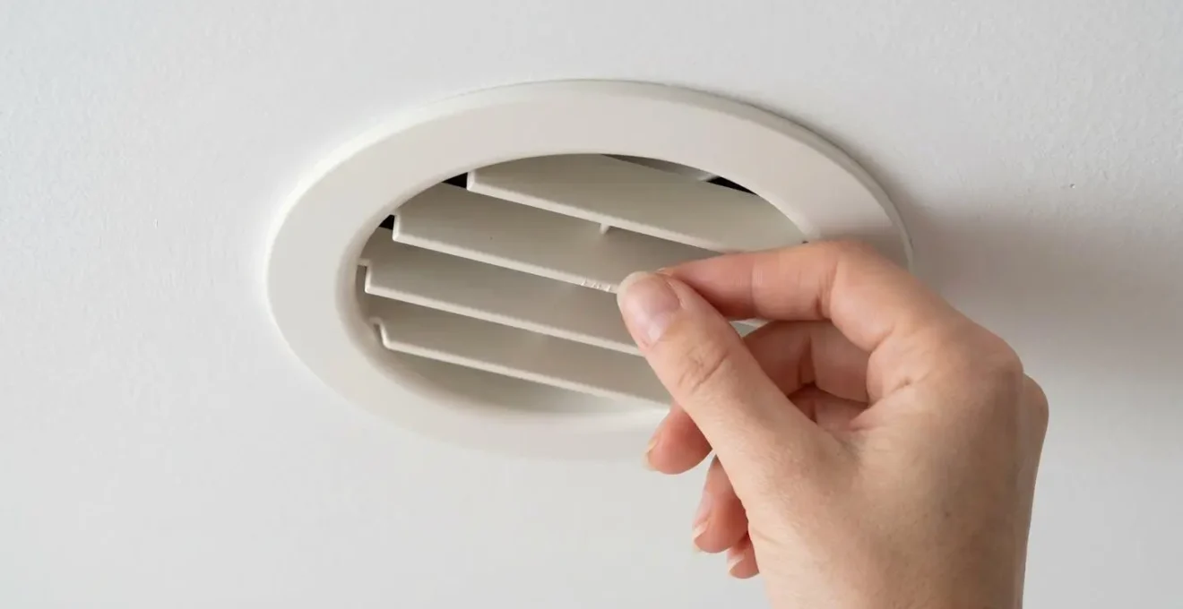 Gros plan sur une bouche de soufflage discrète intégrée dans un plafond blanc, avec diffusion d'air visible
